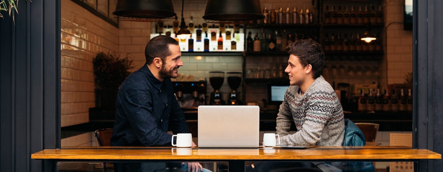 a two men sitting at a table with a laptop